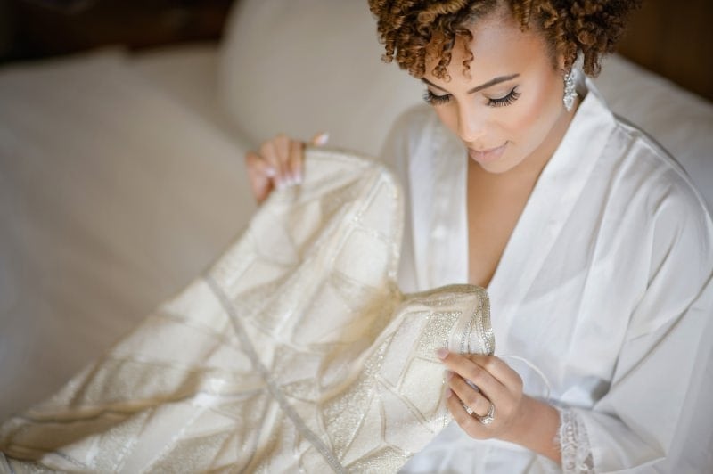 A bride in a white robe admiring her wedding dress.