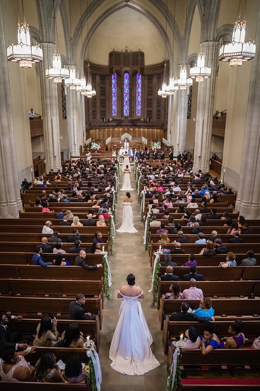 A bridesmaids, captured by wedding photographers, gracefully walks down the aisle of a church in this stunning display of wedding photography.