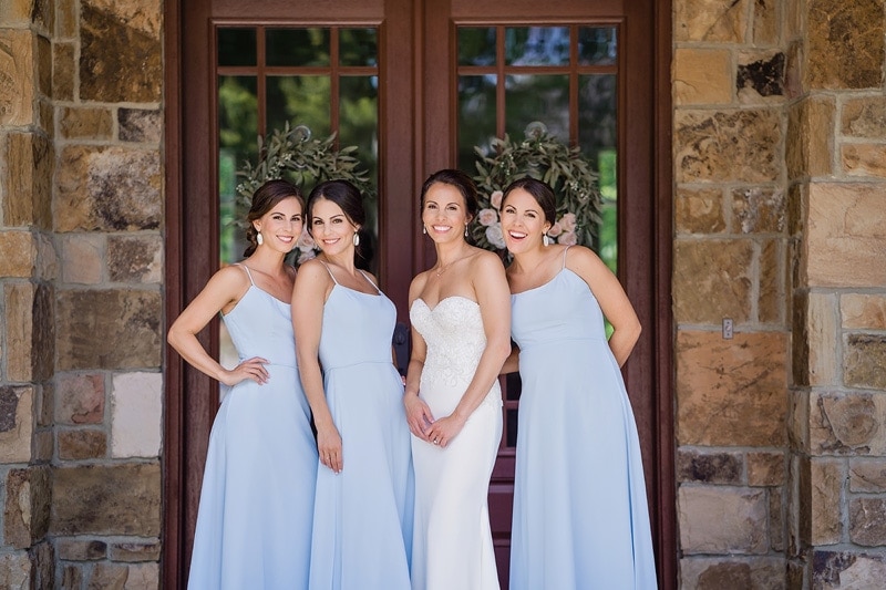 Four bridesmaids in light blue dresses posing for wedding photography in front of a door.