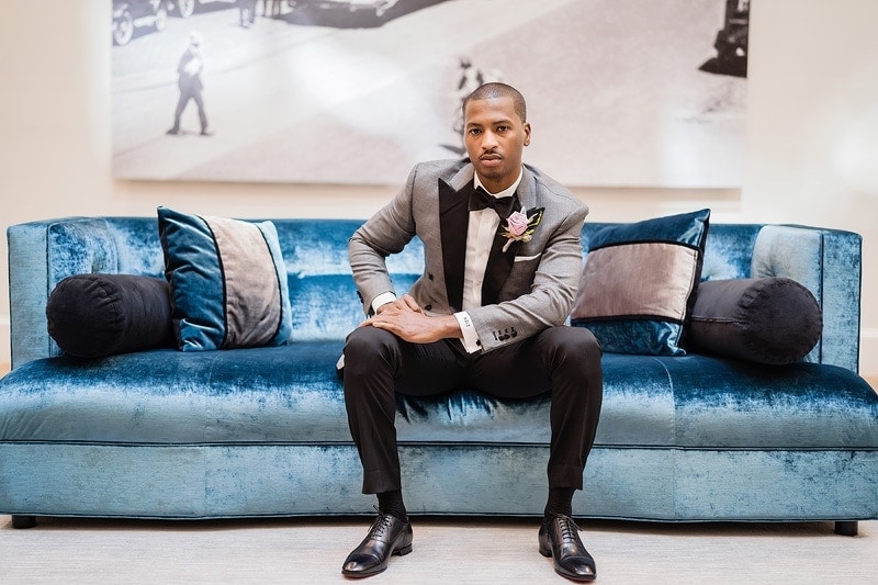 A groom sitting on a blue gallery couch.