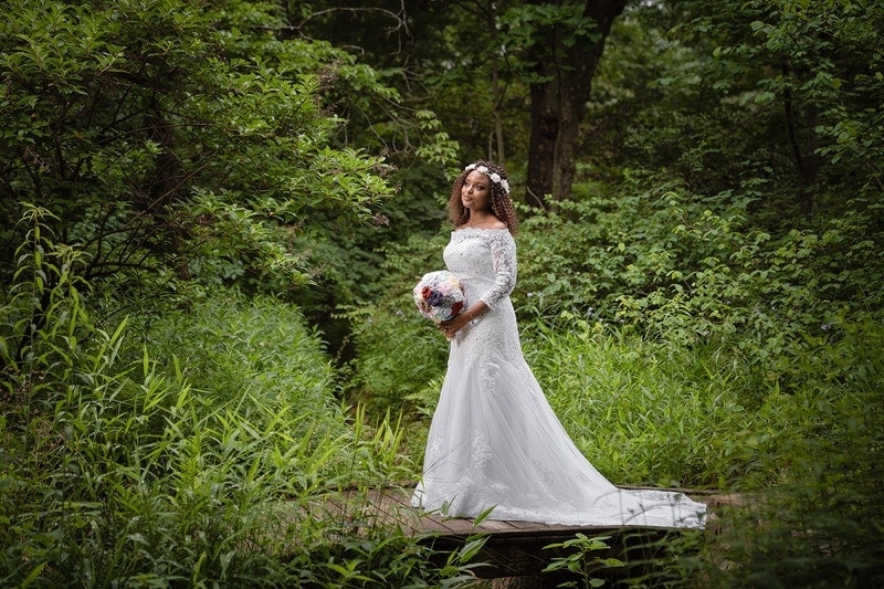 A bride in a wedding dress standing on a bridge in the woods, creating a picturesque scene that would be fitting for any wedding gallery.