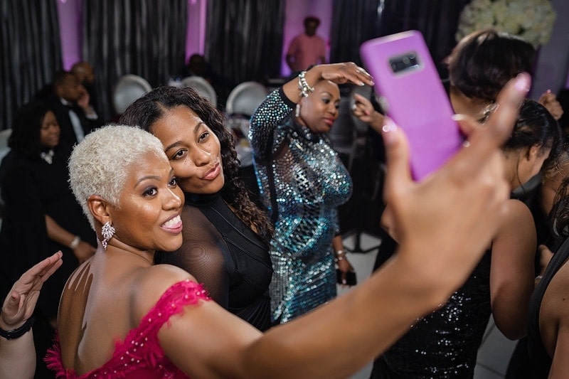 Two women capturing a selfie at a wedding reception, captured by professional wedding photographers.