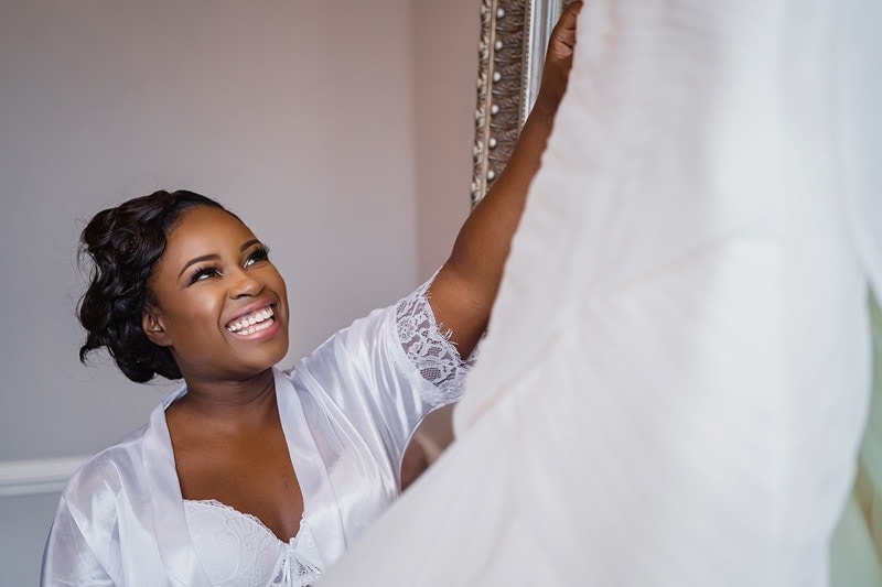 A bride smiling at her wedding dress.