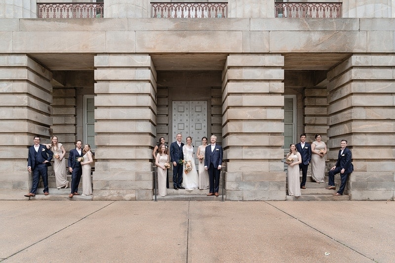 A group of bridesmaids and groomsmen posing in front of a wedding building.