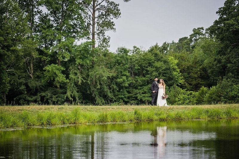 A wedding couple standing in front of a serene pond.