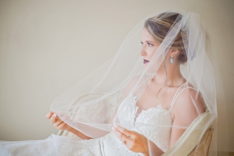 A bride sitting in a chair wearing a veil for her Wedding.
