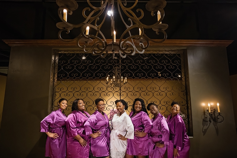 A group of floral bridesmaids in purple robes posing in front of a chandelier.