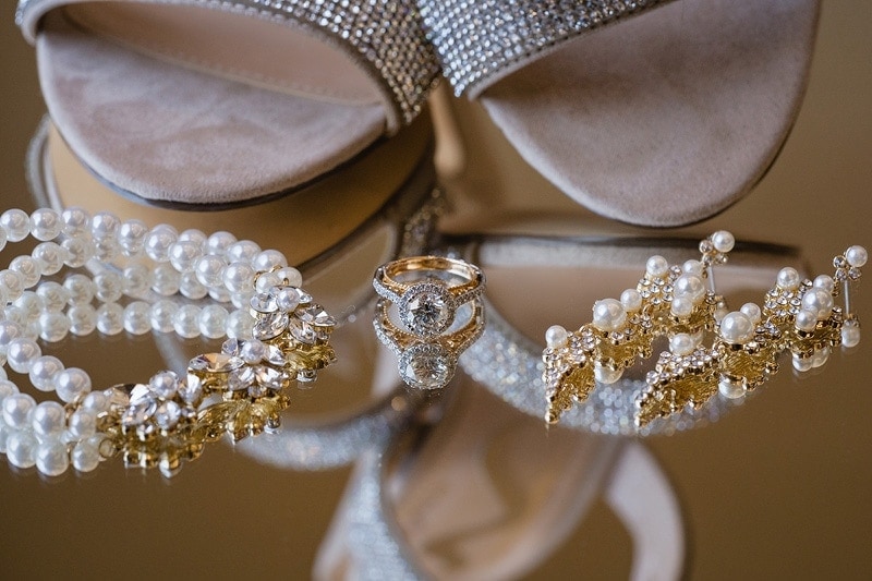 A bride's wedding jewelry and shoes beautifully reflected on a mirror.