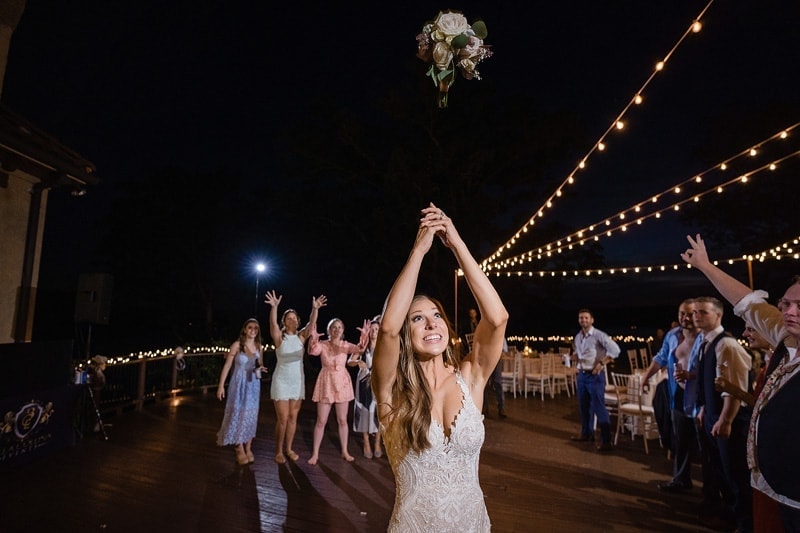 A bride throws her bouquet into the air at a wedding while being captured by wedding photographers.