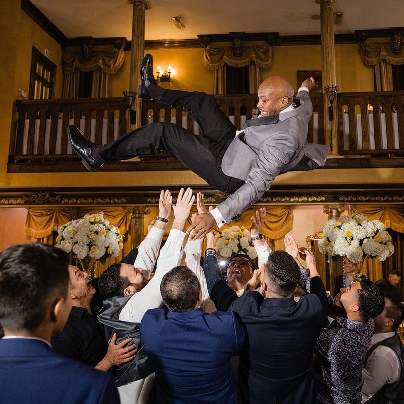 A groom being thrown into the air by his groomsmen during his wedding reception.