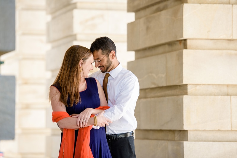 A man and woman embrace in front of a building during their engagement photoshoot with a talented engagement photographer.