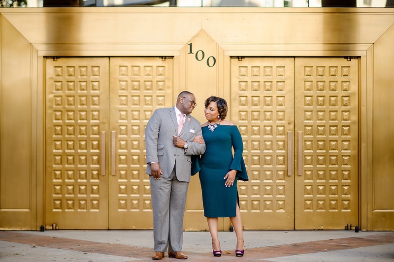 An engagement couple posing in front of a golden door for their engagement photos.