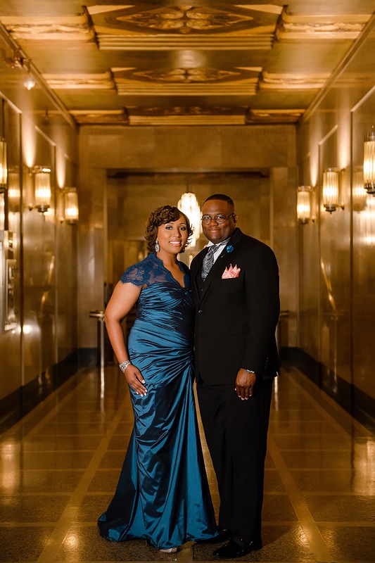 An engagement photographer capturing a man and woman in formal attire during their engagement photoshoot in a hallway.