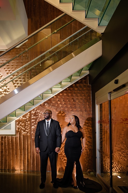 A man and woman, captured by an engagement photographer, standing in front of a staircase for stunning engagement photos.