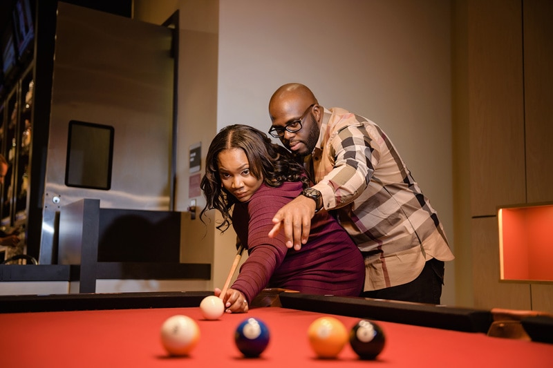 An engagement photographer captures the joyful moments as a couple plays billiards in their room.