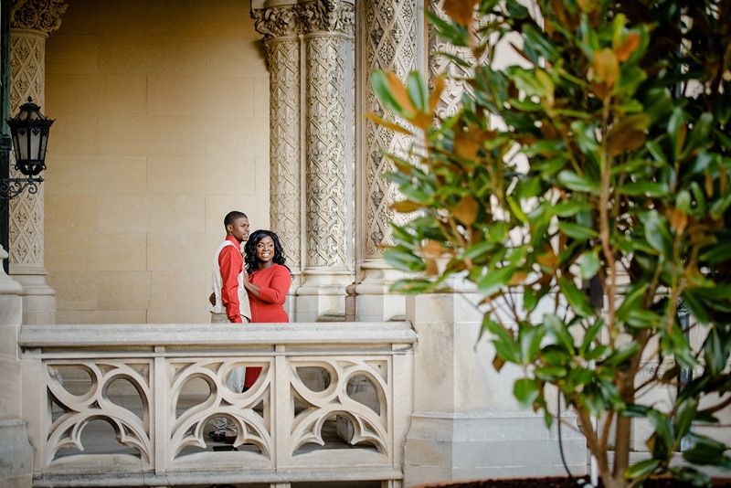 An engaged couple standing on the balcony of an ornate building, captured by a talented engagement photographer for their breathtaking engagement photos.