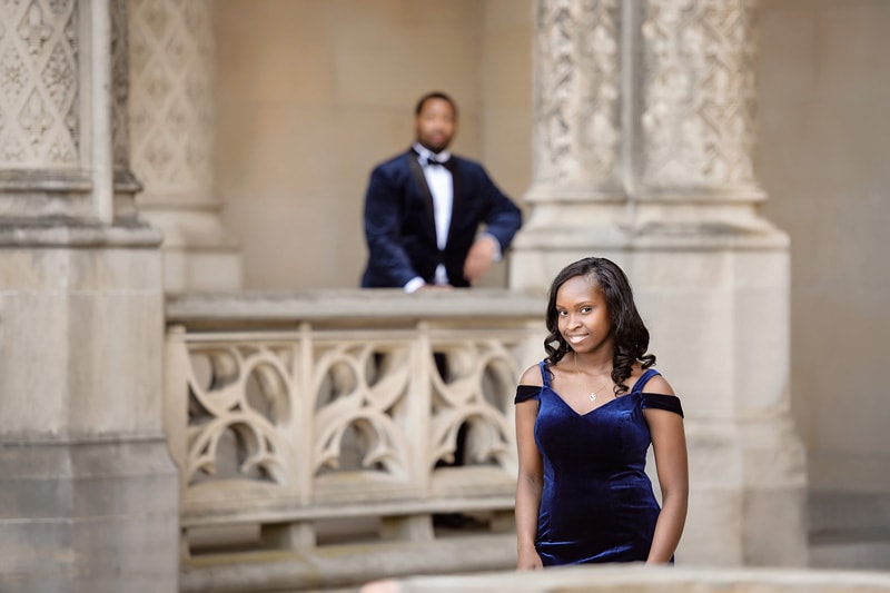 An engaged couple in a blue dress standing on a staircase, captured beautifully by an engagement photographer.