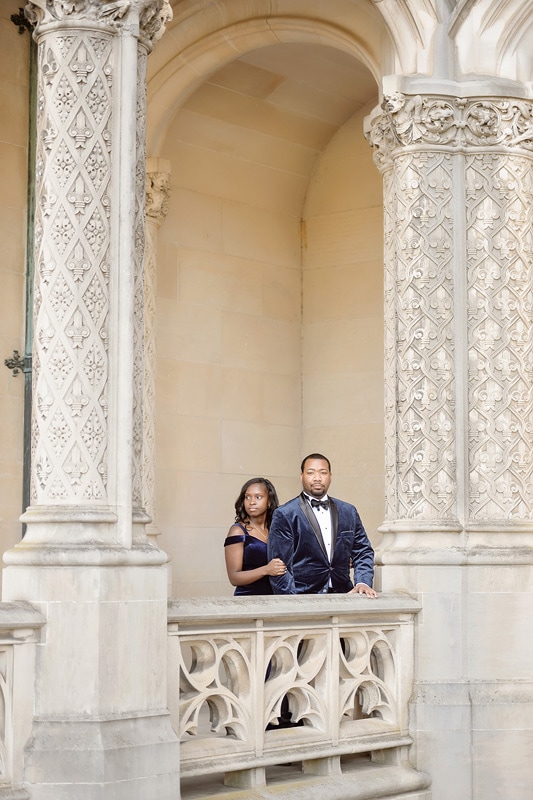 An engaged couple standing on the balcony of an ornate building, captured by an engagement photographer.
