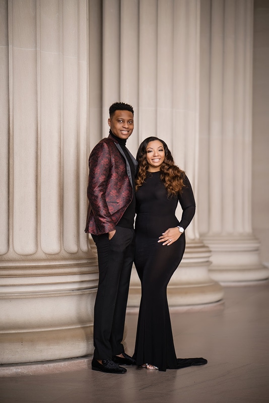 An engagement photographer captures a man and woman posing in front of beautiful columns, creating stunning engagement photos.