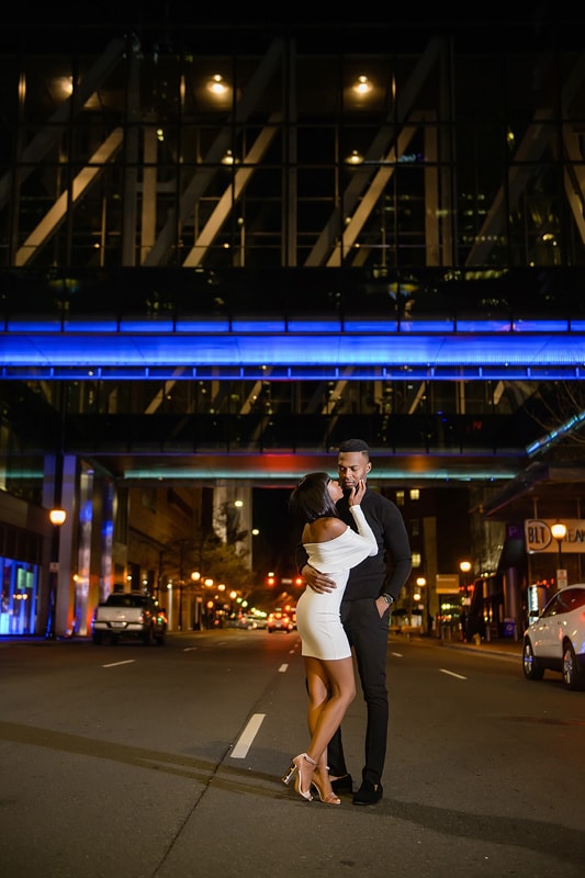 An engagement photographer captures a couple embracing in front of a building at night for their engagement photos.