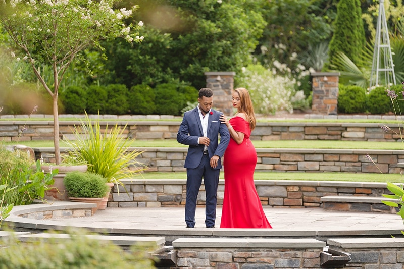 An engagement photographer captures a man and woman in a red dress standing in a garden, creating timeless engagement photos.