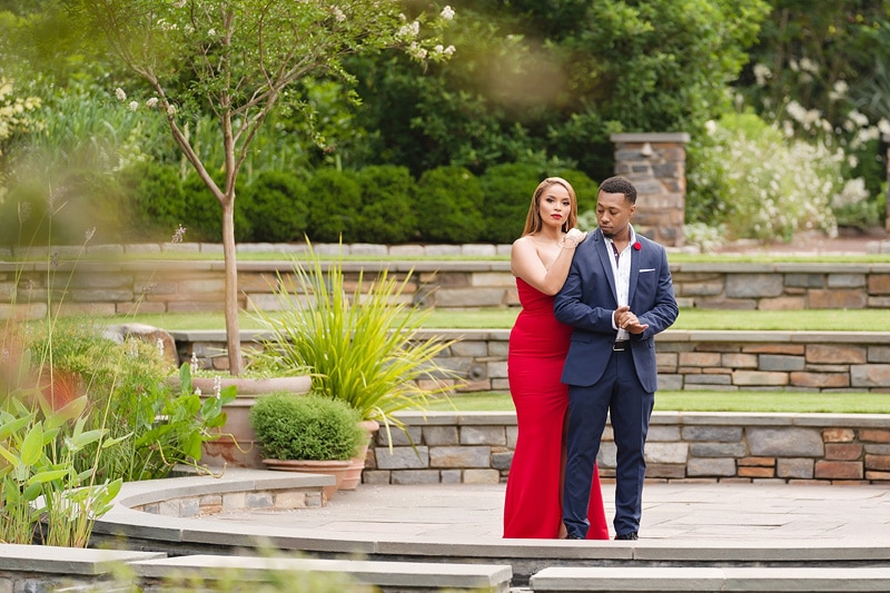 An engaged couple in a red dress standing in a garden, captured beautifully by an engagement photographer during their engagement photoshoot.