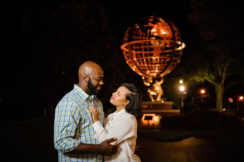 An engaged couple embracing in front of a globe at night during their engagement photoshoot.
