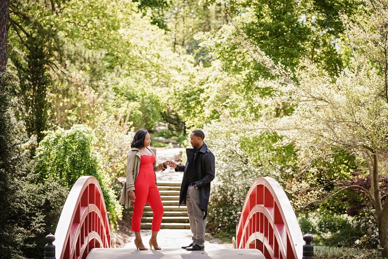 An engaged couple standing on a bridge in a garden, captured by an engagement photographer.