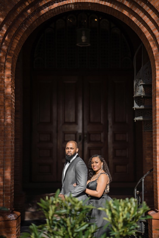 An engaged couple posing in front of a brick building, captured by an engagement photographer.