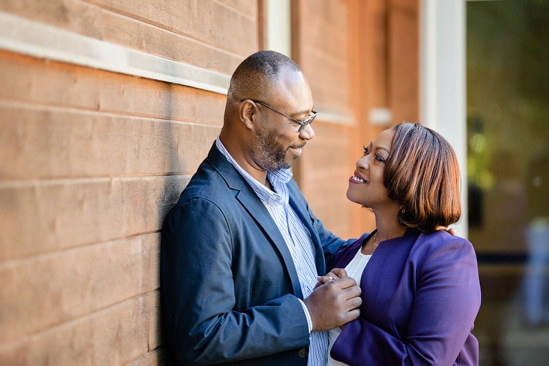 A black couple posing for engagement photos leaning against a brick wall.