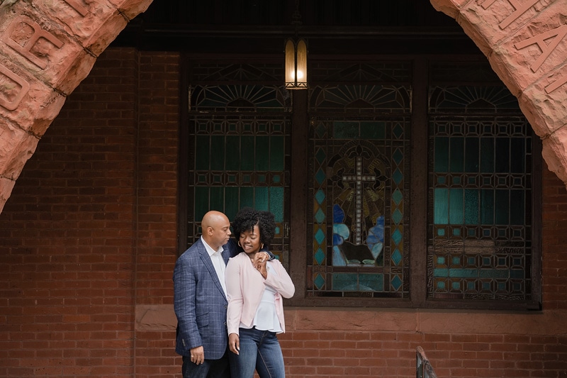 A couple having their engagement photos taken in front of a red brick building by an engagement photographer.