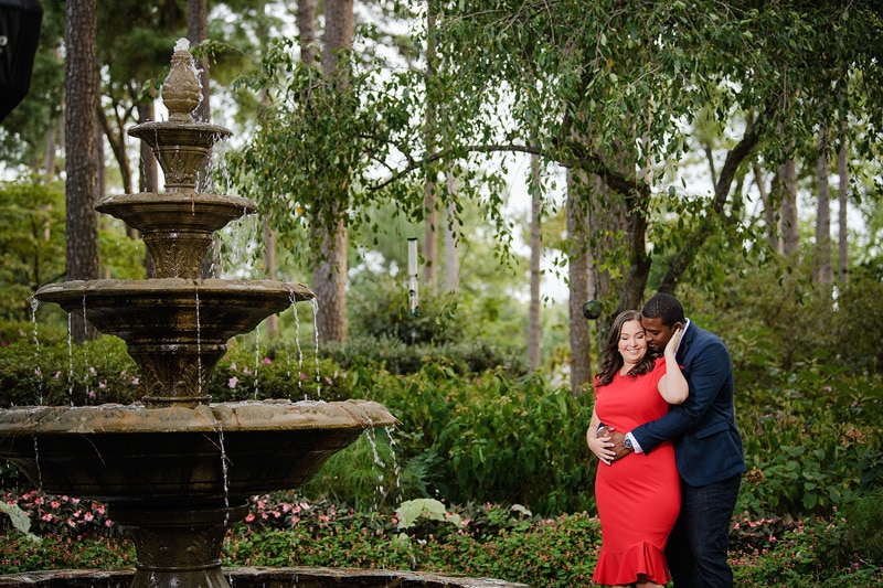An engaged couple embracing in front of a fountain during their engagement photography session.
