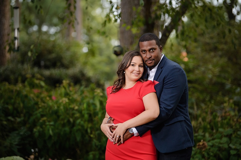 An affectionate couple in a red dress capturing their engagement photos embracing in a garden, with the skillful eye of an engagement photographer perfectly preserving each cherished moment for their engagement photography portfolio.