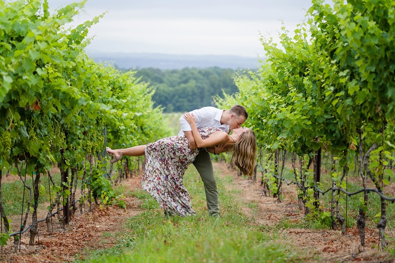 An engaged couple sharing a heartfelt kiss during their engagement photoshoot in a picturesque vineyard.