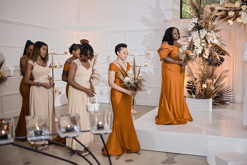 A group of bridesmaids in orange dresses posing with the bride at a magical distillery wedding.