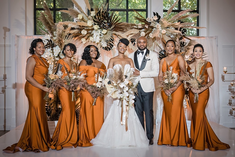 At the distillery wedding, a group of bridesmaids in orange dresses pose for a photo.