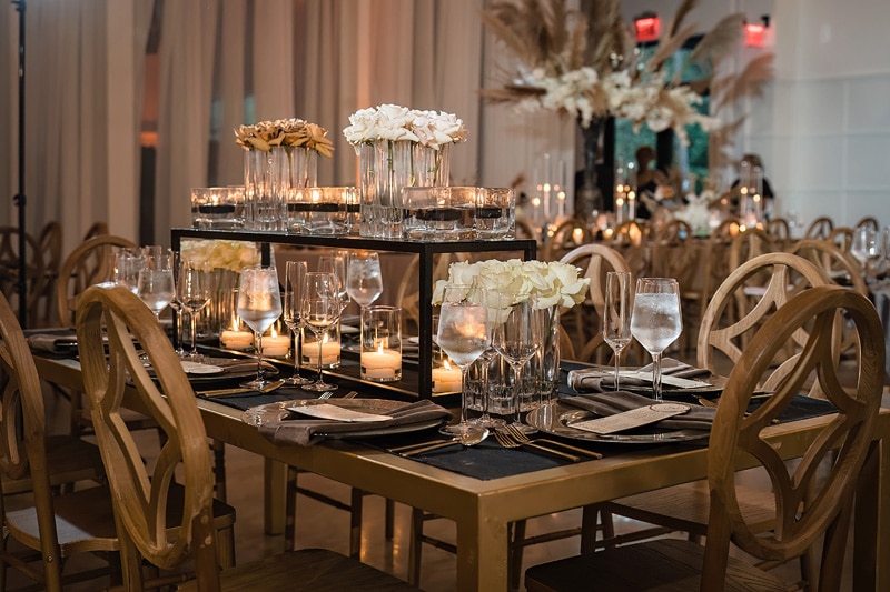 A gold and black table setting with candles and flowers at the distillery wedding.
