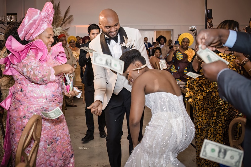 At a lavish wedding held at The Distillery, a stunning bride and groom joyfully shower each other with money, creating an exuberant atmosphere of celebration.