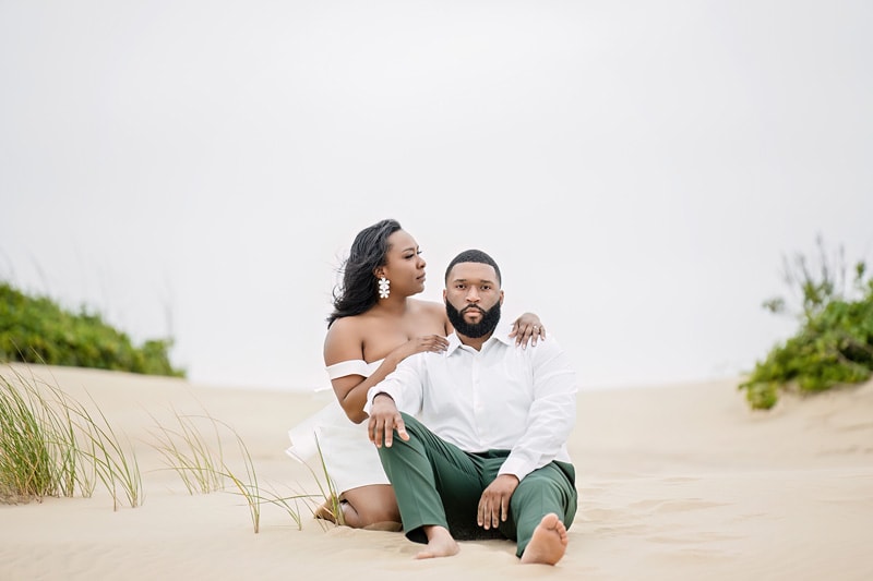 An engaged couple sitting on an Outer Banks sand dune, capturing stunning engagement photos.