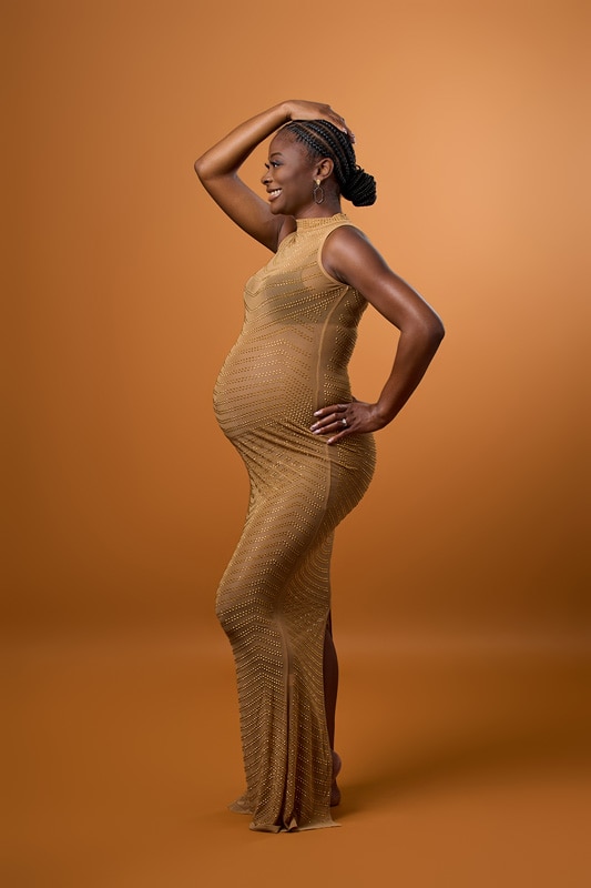 A pregnant woman in a beige dress posing for a maternity photo.