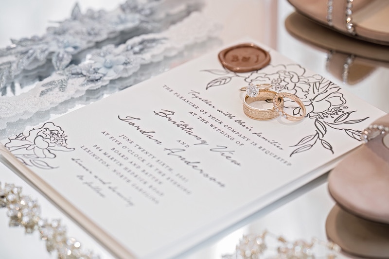 An elegant wedding invitation adorned with rings and a seal from Board & Batten Events Wedding.