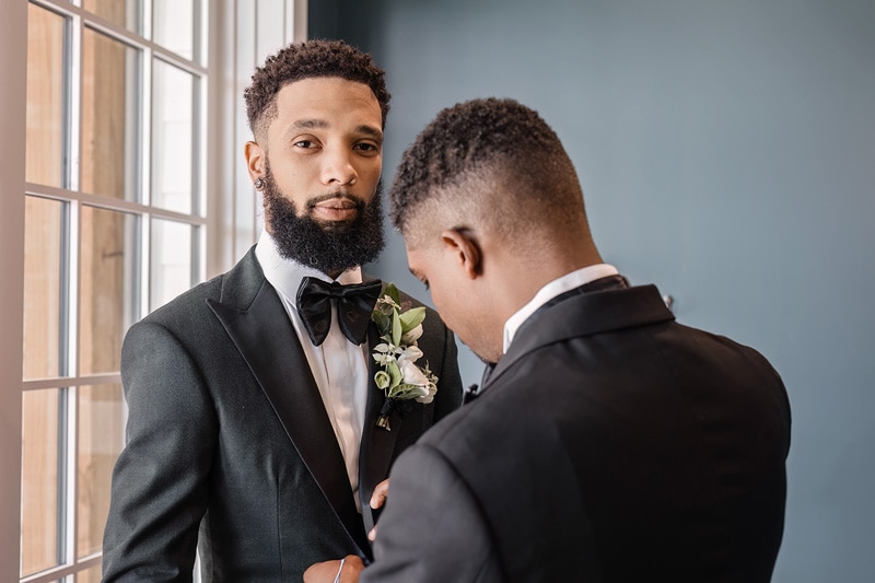 At a Board and Batten Events Wedding, a man in a tuxedo carefully adjusts another man's tie.