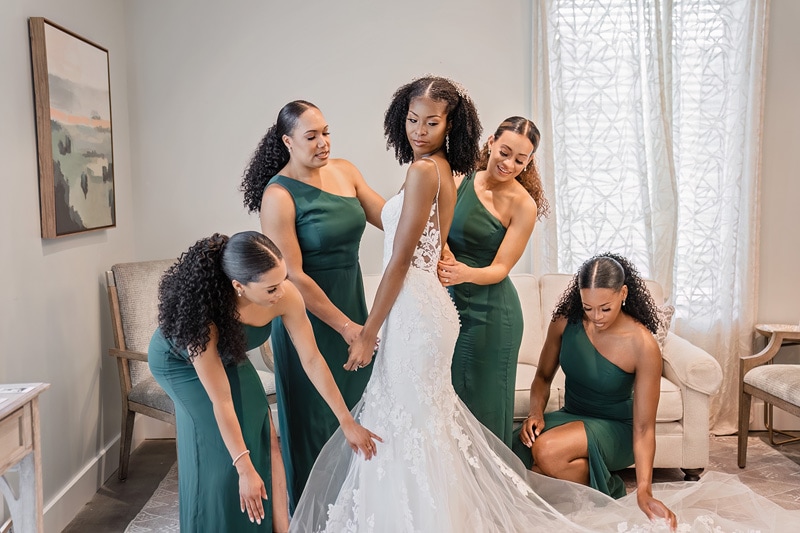 A group of bridesmaids assisting a bride in a green dress at a Board and Batten Events wedding.