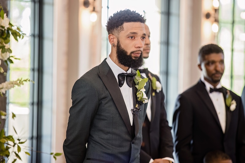 A man in a tuxedo elegantly walks down the aisle at a Board and Batten Events Wedding.