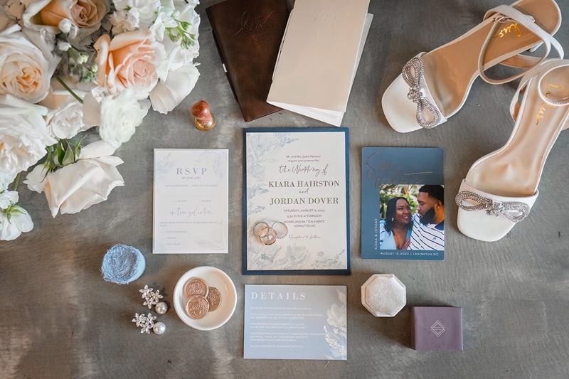 A wedding invitation and shoes are laid out on a table at Board & Batten Events.