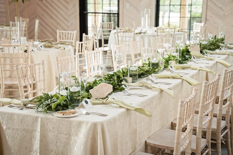 A wedding reception table set with white linens and greenery at the Board & Batten Events venue in Lexington.