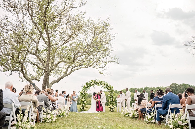 A wedding ceremony under a tree in a field at Board & Batten Events.