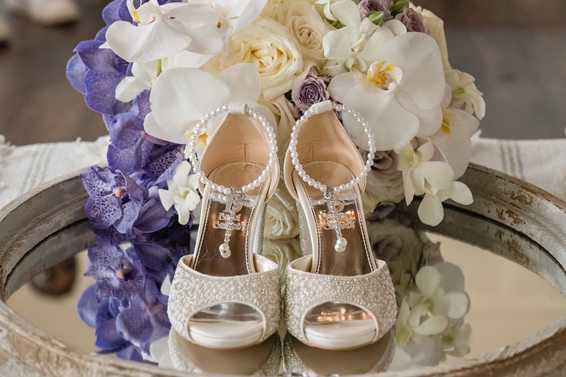 A pair of Pinehill Pavilion wedding shoes on a table next to a bouquet of flowers.