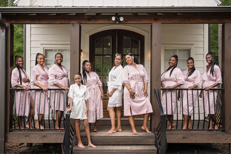 A group of bridesmaids in pink robes posing on the porch at Pinehill Pavilion Wedding.