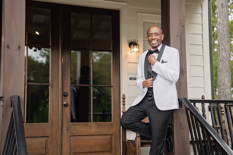 A man in a tuxedo standing on the porch of Pinehill Pavilion, a wedding venue.